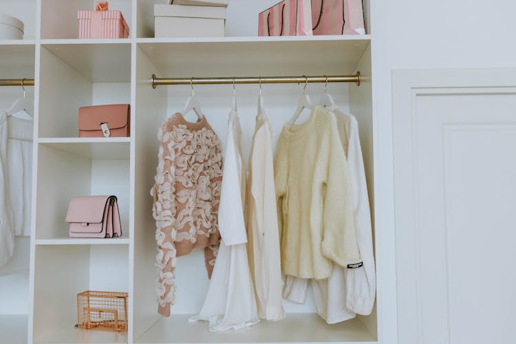 A white closet with clothes on hangers and purses