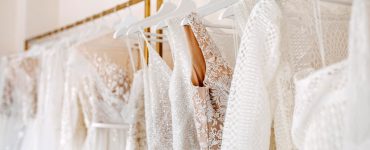Collection of wedding gowns featuring lace, sequins, and embroidered details displayed on a boutique clothing rack.