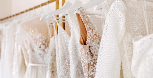 Collection of wedding gowns featuring lace, sequins, and embroidered details displayed on a boutique clothing rack.